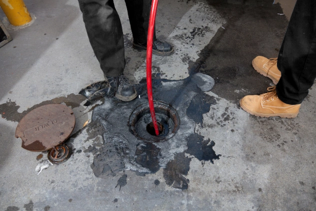 Technician using a red hose for hydro jetting in a manhole.