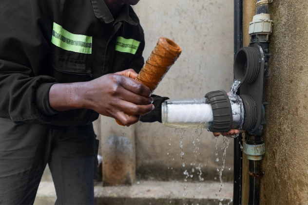 Plumber repairing a leaking pipe and adjusting a filter, with water flowing out.