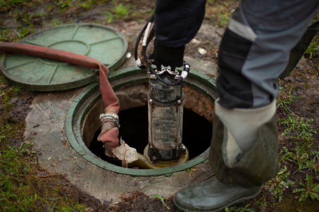 Worker using pump to clean cesspool with protective boots and gear.