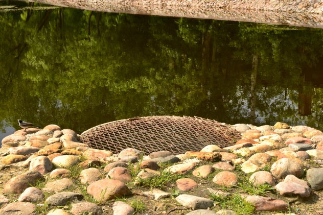 Stone pathway with a circular metal cover near water.