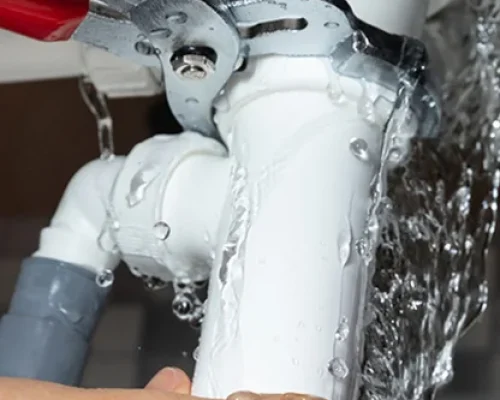 Plumber fixing a leaking pipe with a wrench, with water flowing from the pipe.