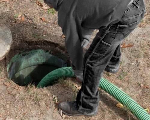 Worker preparing to pump septic tank with green hose.